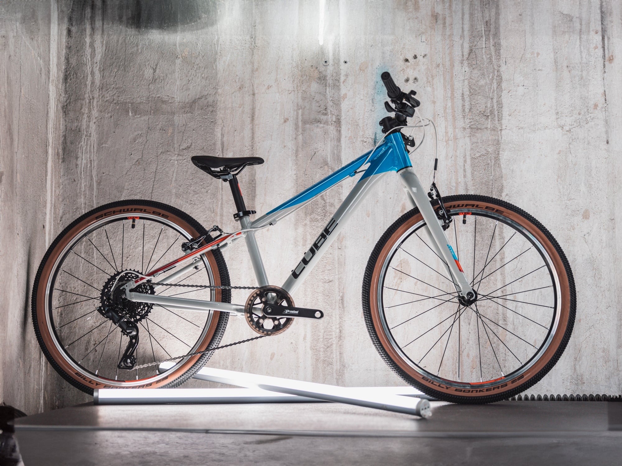 Ein silber-blaues Cube Kinderfahrrad steht vor einer Betonwand