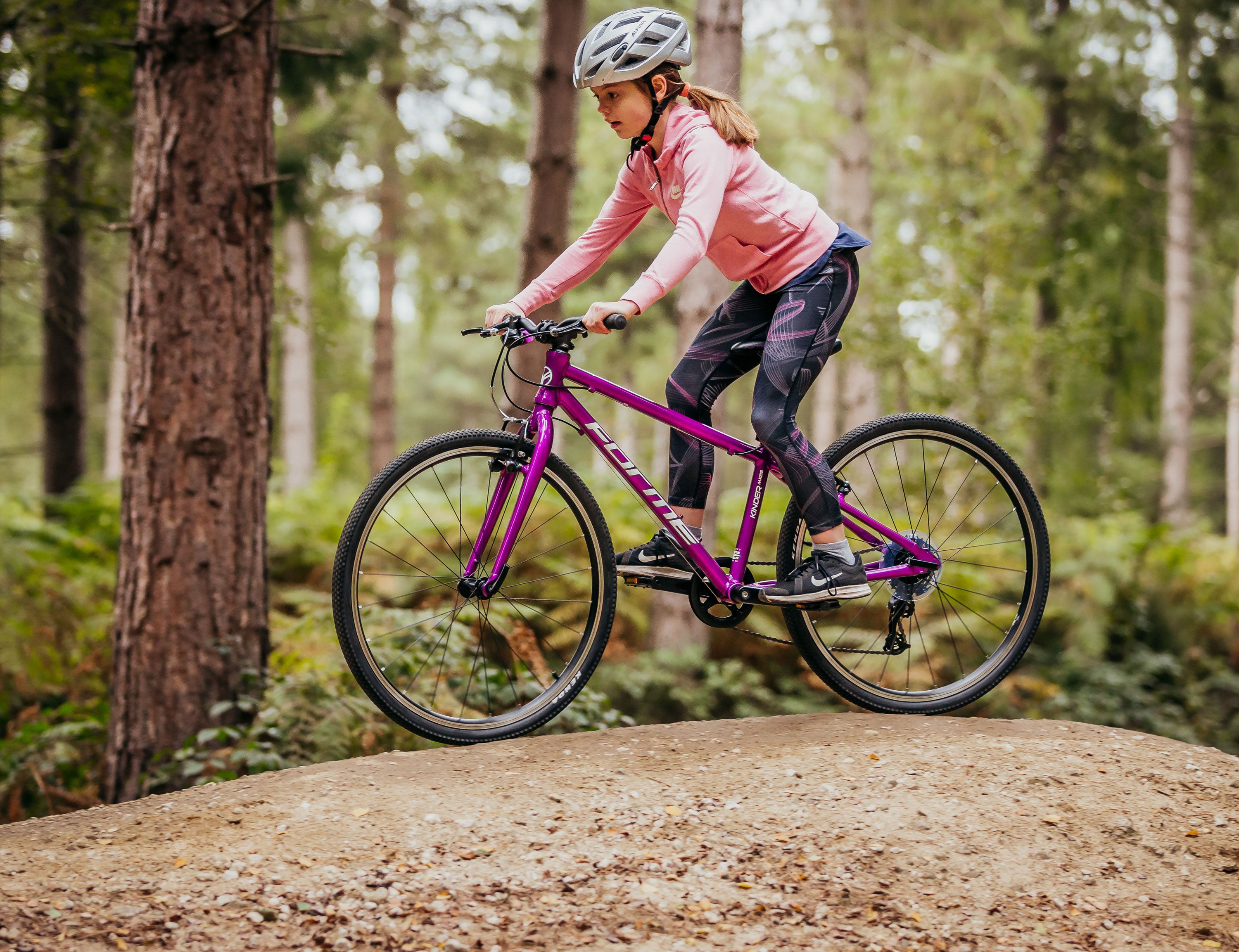 Ein Mädchen fährt auf ihrem lilafarbenen Kinderfahrrad Forme Kinder 26 im Wald