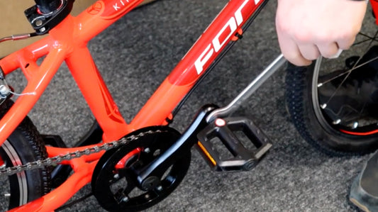 Die Pedale eines Orangenen Fahrrads wird mit einem Schraubenschlüssel festgezogen