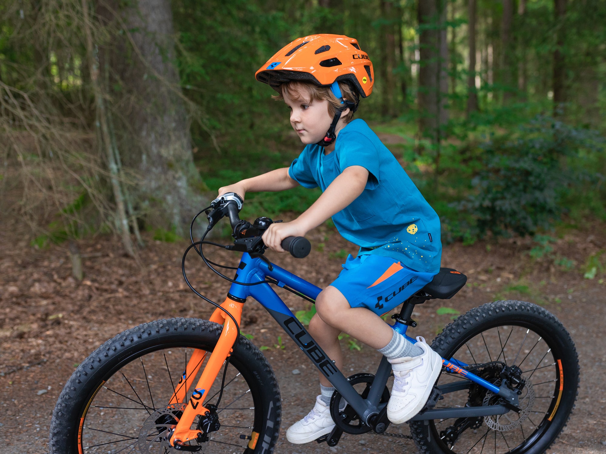 Ein junge in blauer Sportkleidung und einem orangenen Fahrradhelm fährt auf seinem Cube Kinderfahrrad durch einen Wald