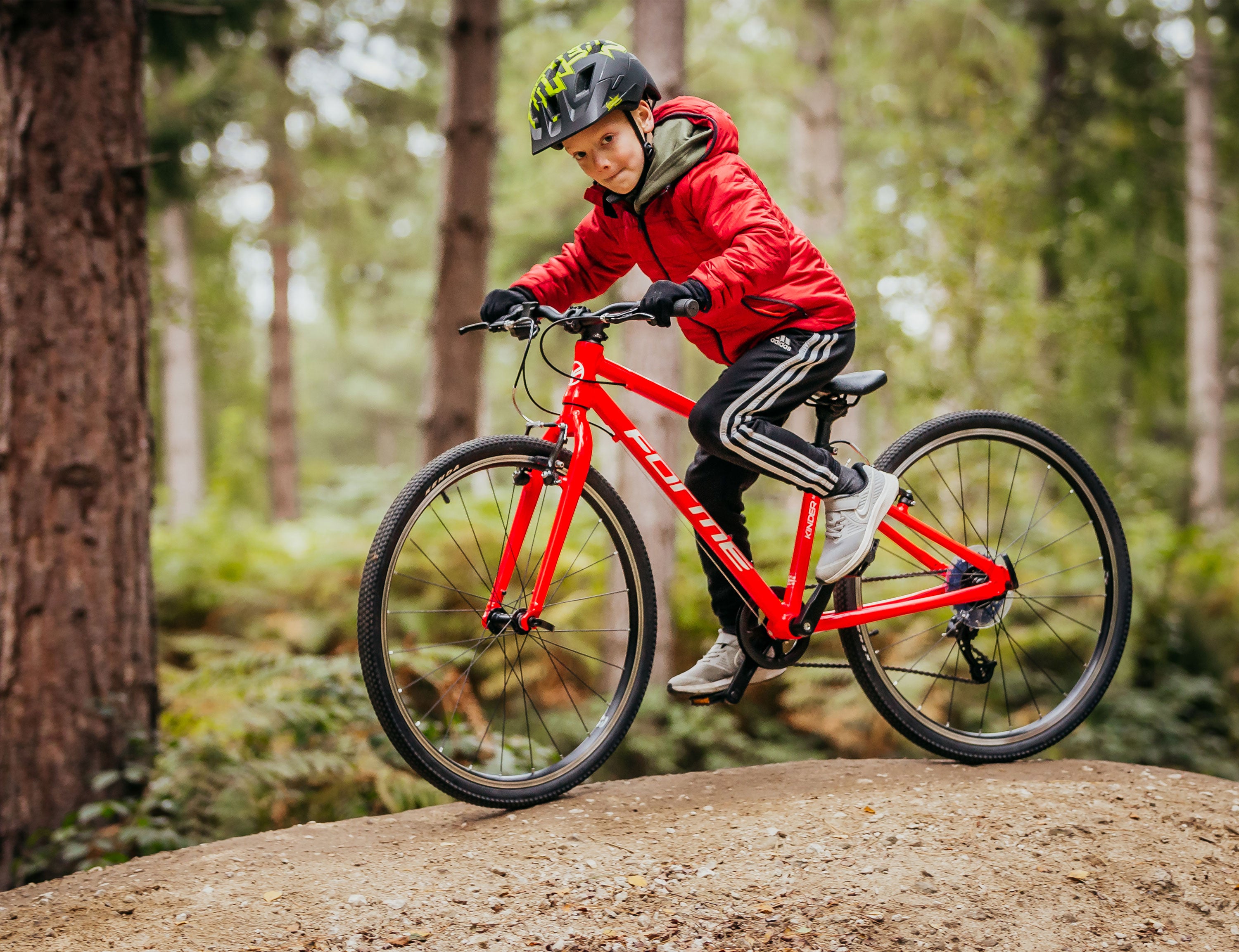 Ein Junge fährt auf seinem roten Kinderfahrrad Forme Kinder 24 im Wald