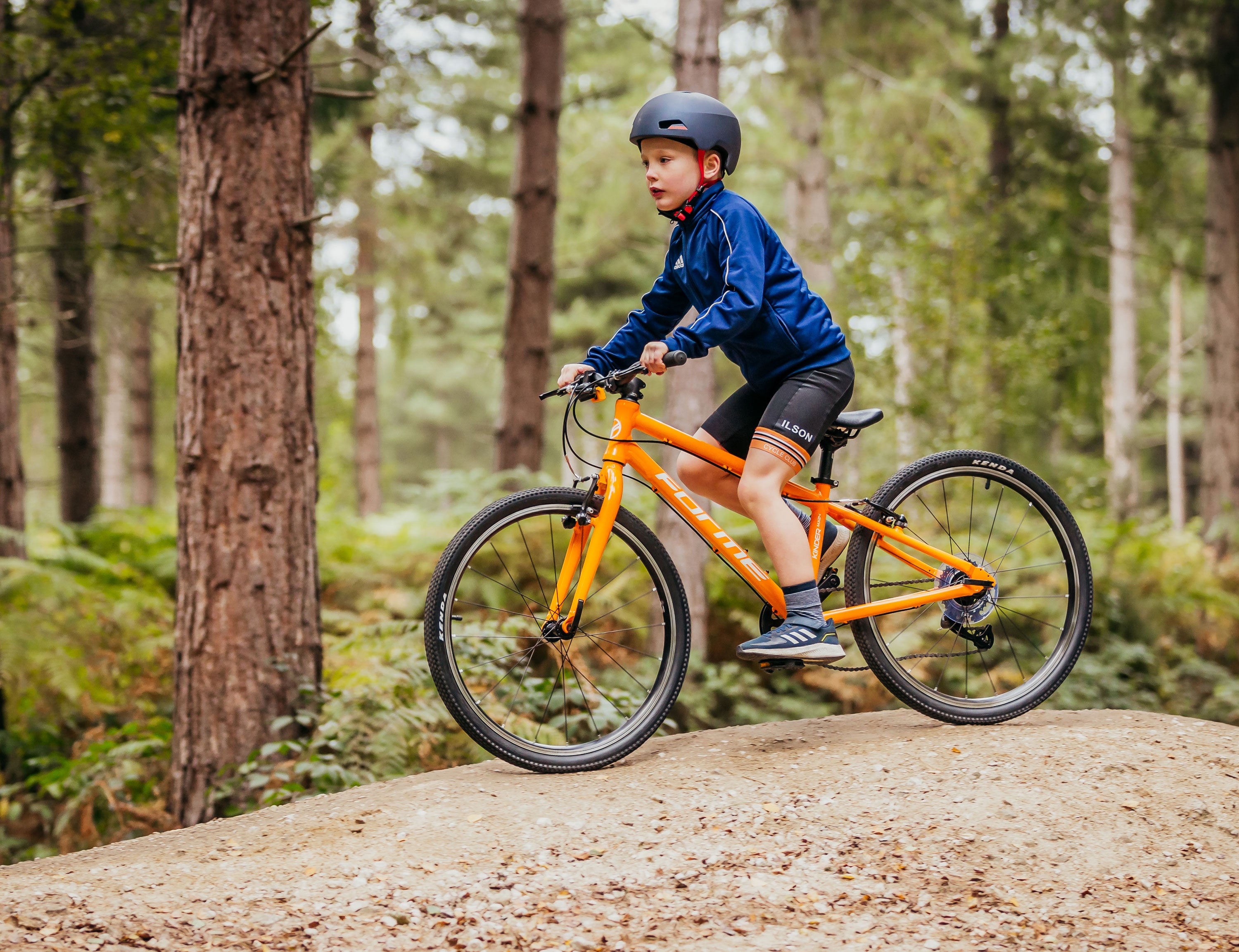 Ein Junge fährt auf seinem orangefarbenen Kinderfahrrad Forme Kinder 20 im Wald